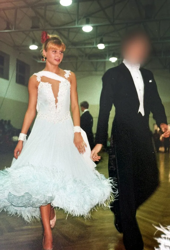 Justyna as a junior competitor in a white ballroom dress with feathers, walking onto the floor with her partner
